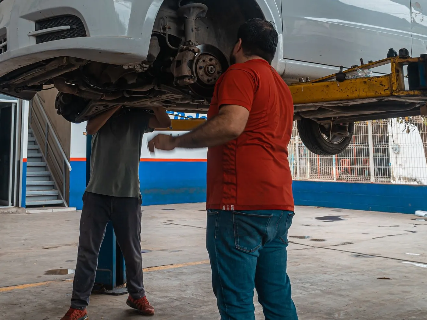 Zwei Mechaniker arbeiten an einem Fahrzeug auf der Hebebühne in einer hellen Werkstatt